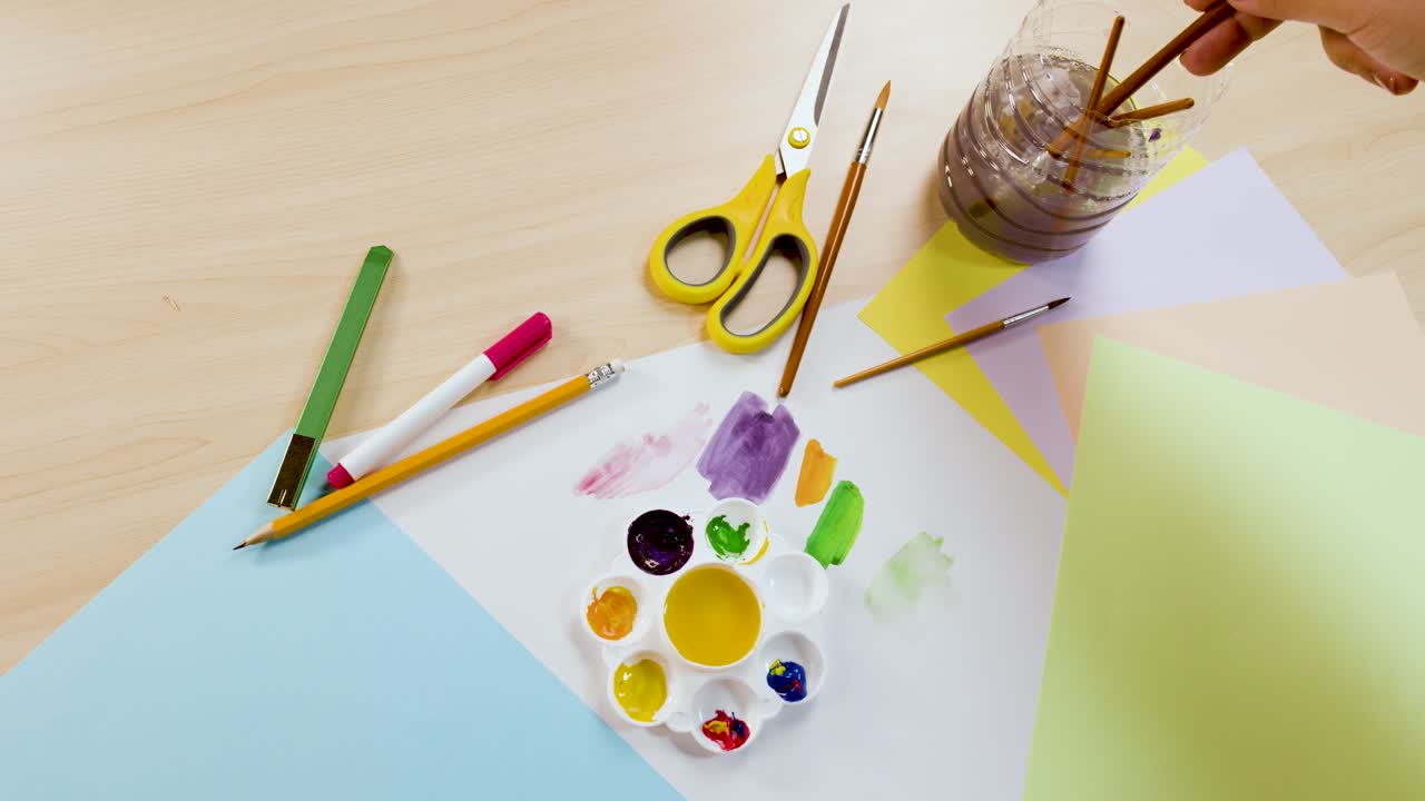 Overhead shot of an artist mixing violet paint on a palette surrounded by art supplies
