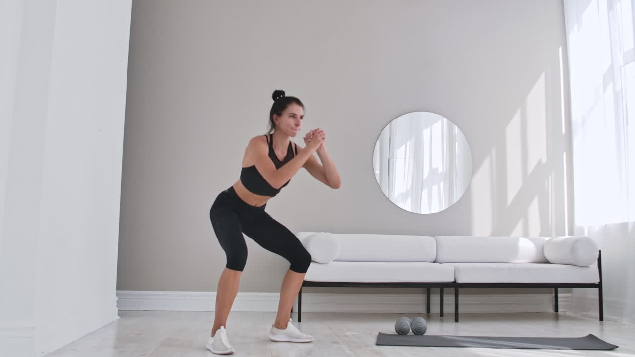 Woman exercising jumping squats in home. Healthy female in sportswear doing jumping squats at home. Woman exercising at living room