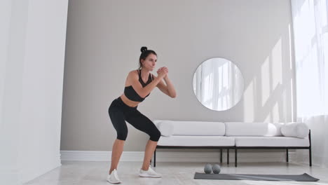 mujer haciendo sentadillas saltando en el hogar. mujer sana en ropa deportiva haciendo sentadilla saltando en la casa. mujer haciendo ejercicio en la sala de estar