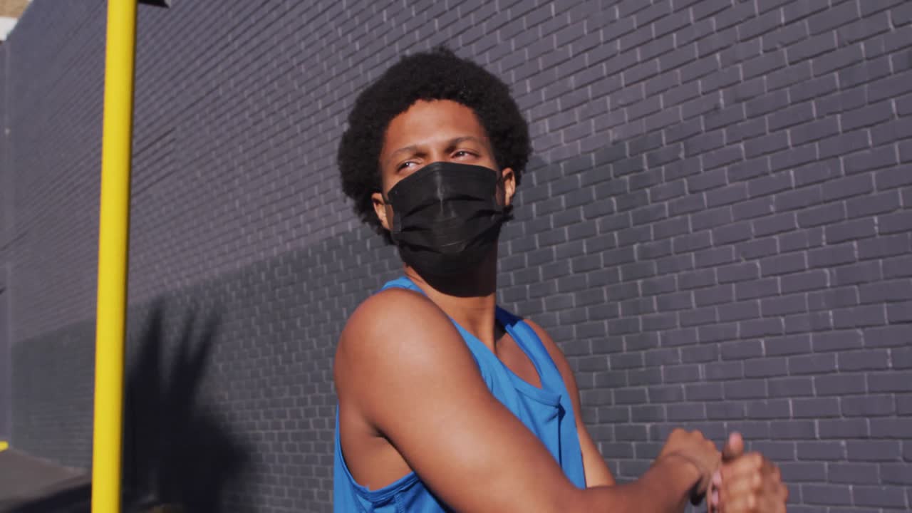 hombre afroamericano en forma haciendo ejercicio en la ciudad usando máscara facial, estirándose en la calle