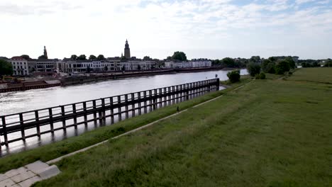 vast dutch landscape aerial following male trail runner along river ijssel in floodlands with countenance of tower town zutphen behind