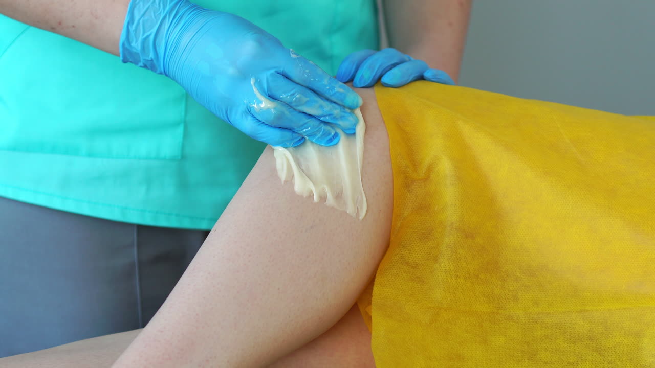 la chica habla por teléfono y sonríe durante la depilación de las piernas en el salón de belleza. depilación de las piernas con azúcar. clouse-up