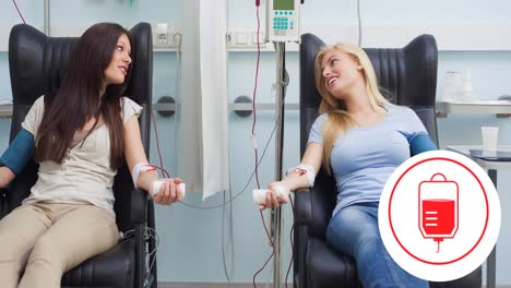 Animation-of-blood-bag-symbol,-over-two-talking-female-donors-giving-blood