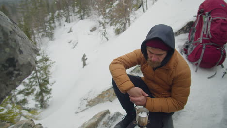 man melting ice on gas stove during winter camping in mountains