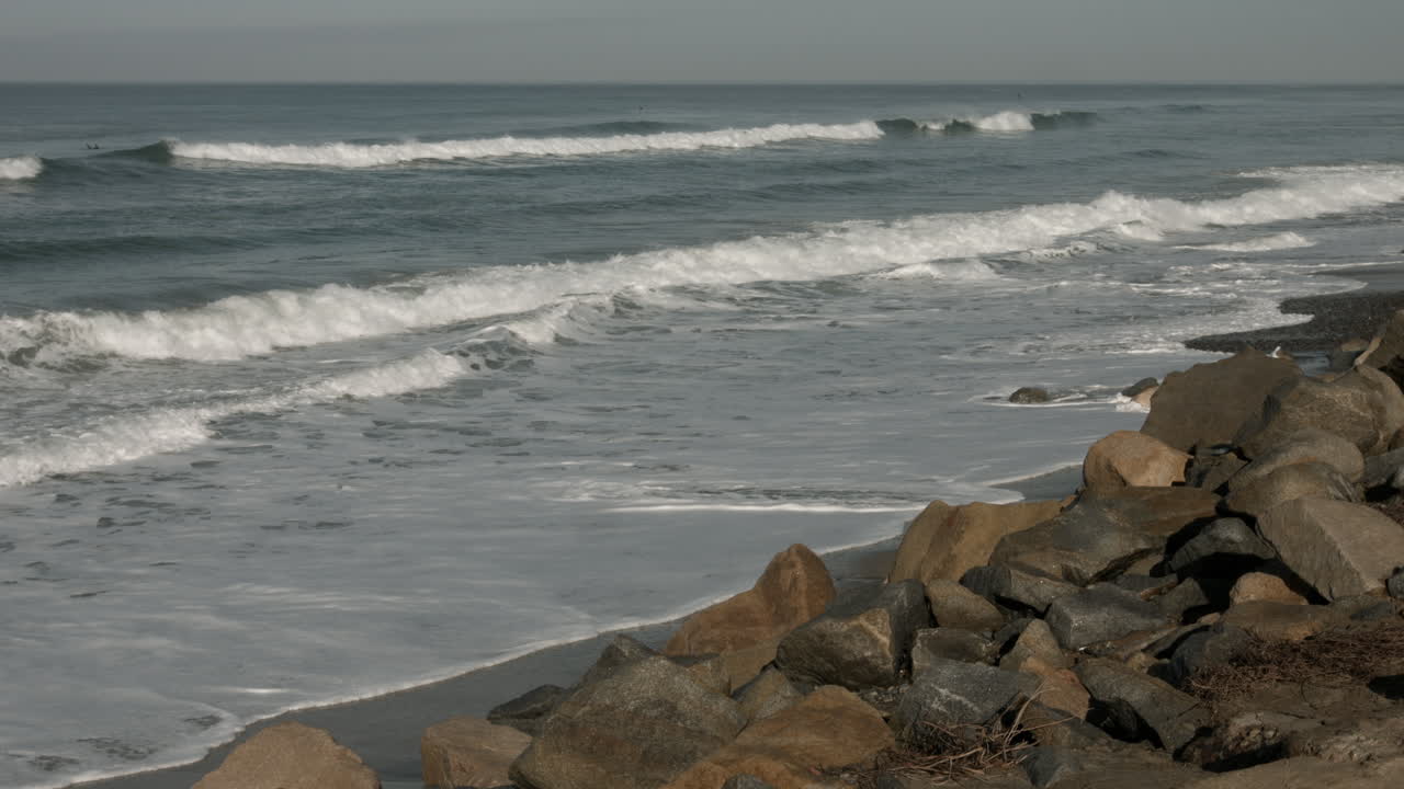 las olas chocan contra la playa mientras un surfista monta una ola en el parque estatal torry pines en california.