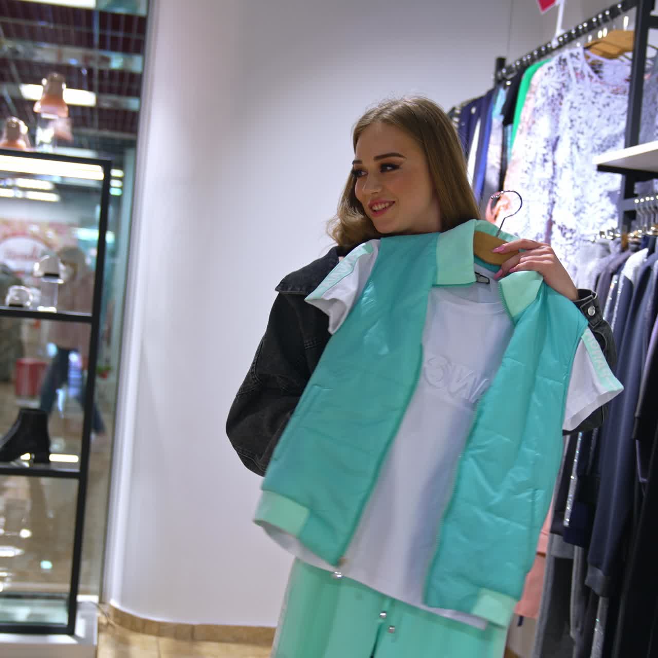Pretty positive smiling girl holding a sport suit apposing it to her body. Lady looks at clothes closely showing it to somebody