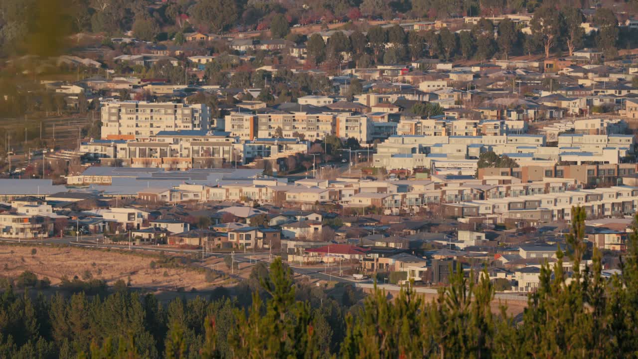 A slow zoom out reveals newly built townhouses and expanding infrastructure in a Canberra suburb during sunrise