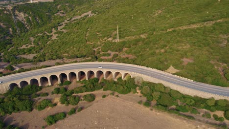 aerial view following car traffic moving over bridge during daytime, an stone arch bridge in the mountains north of the coastal town of tarifa in andalusia, spain