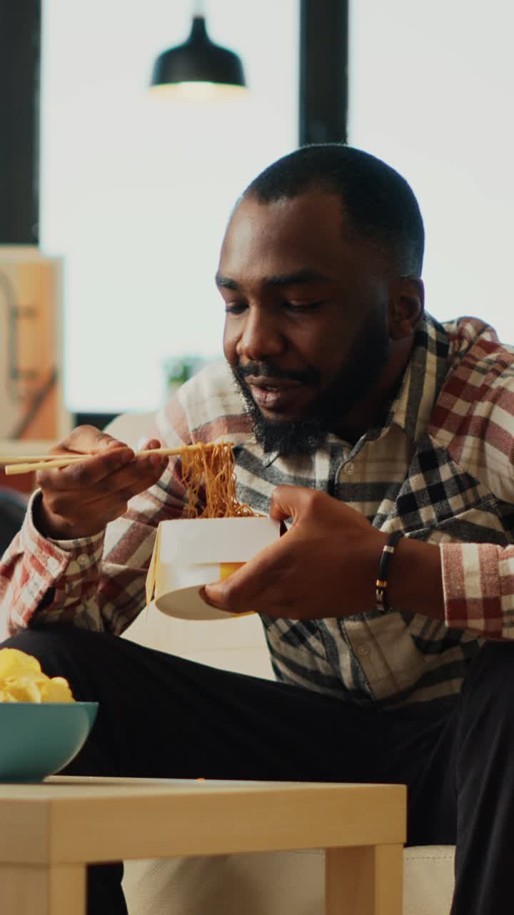 Vertical video: Happy guy eating noodles with chopsticks at home