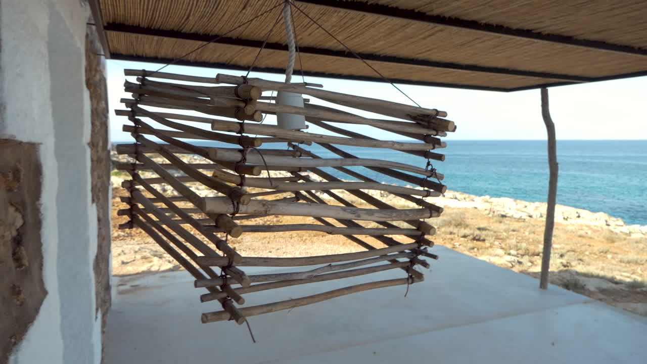lámpara hecha a mano con trozos de madera y alambre de metal meciéndose con el viento frente al océano.