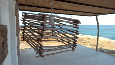 lámpara hecha a mano con trozos de madera y alambre de metal meciéndose con el viento frente al océano.