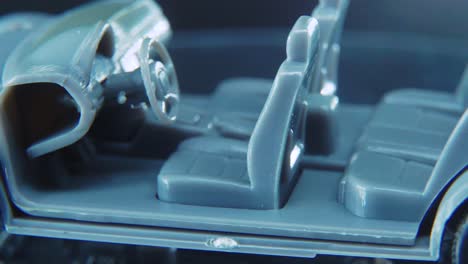 a tiny model metal sample skeleton of a car on a rotating stand with studio lights, macro close up shot, 4k video, silver wheels, black tires, doors and windows, plastic seats