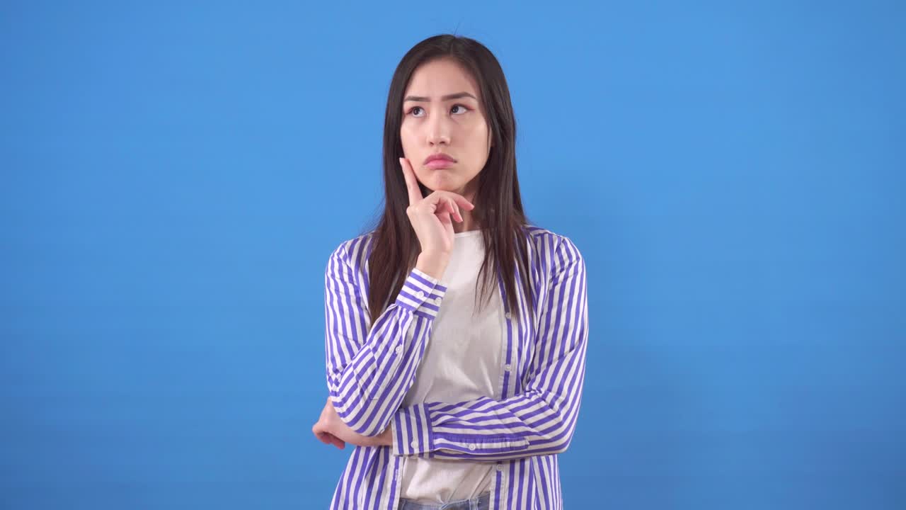 una joven asiática pensativa con una camisa de pie sobre un fondo azul