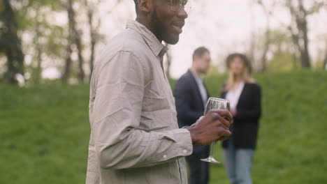 close up view of an middle aged man dancing while holding a wine glass in the park