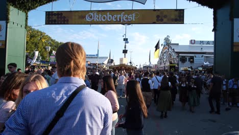 people dressed in traditional dirndl and lederhosen enter the oktoberfest grounds, passing beneath an archway marked “oktoberfest,” ready to join the lively festivities inside.