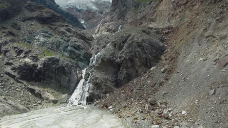 aerial-flight-close-to-wild-waterfall-going-down-a-massive-mountain-front,-breathtaking-drone-shot-over-swiss-alps-in-saas-fee