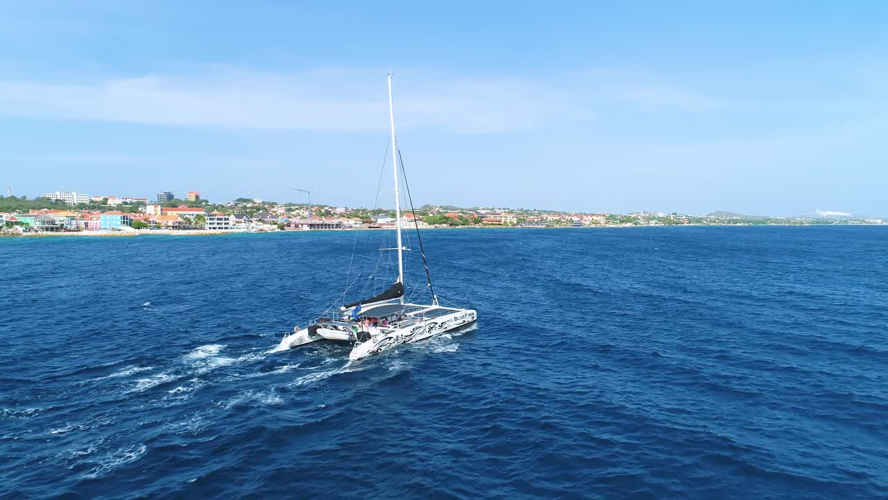 정오 에 푸른 바다 파도 를 가로질러 흔들리는 카타마란, 드론 이 뒤에서 따라온다
