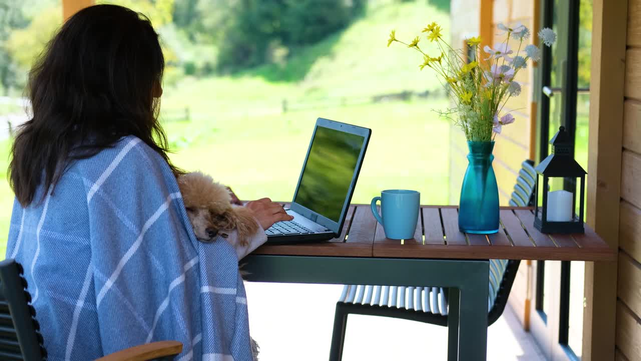 산의 오두막에서 컴퓨터에 앉아 일하는 젊은 프리랜서 여성.