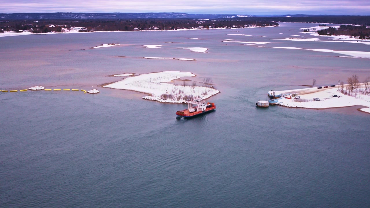 Aerial perspective of a car ferry traveling through a snow-covered winter environment.