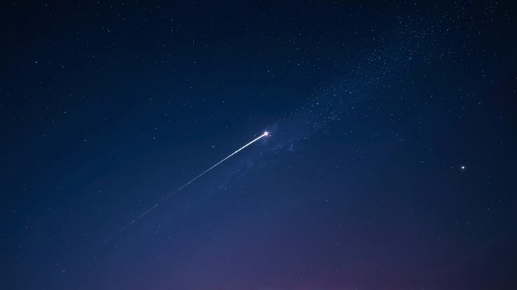 Shooting meteor entering air racing across night above horizon, with trail among stars, copy space