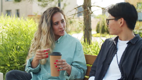 mujer sosteniendo café y hablando con una colega en el parque