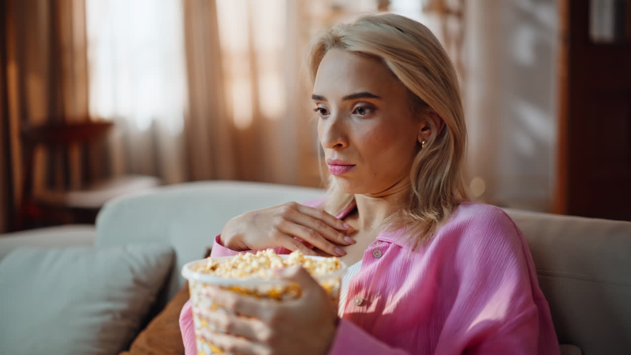 Ragazza tesa si rilassa sul divano di una casa moderna guardando uno show televisivo, primo piano. Donna spaventata
