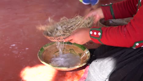 woman filtering the root pieces of plant out of the soap on the bowl. - close up