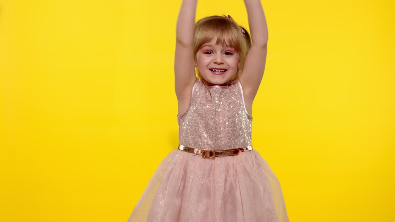 hola o adiós. pequeña niña rubia sonriente niño niña saludando con la mano en fondo amarillo