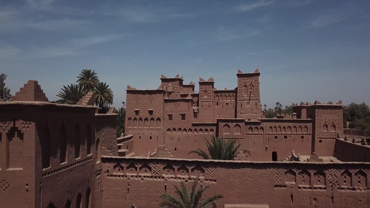 Zoom indietro che rivela i complessi tetti a strati e le torri di una Kasbah tradizionale a Ouarzazate. Il movimento della camera stabilisce la scala e la densità dell'architettura della fortezza di terra