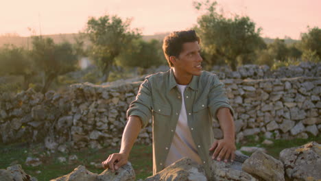 relaxed guy leaning stone wall at nature. smiling man looking camera vertical