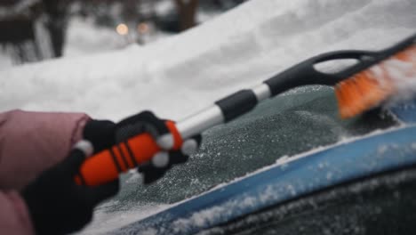 removing snow from a car windshield in winter