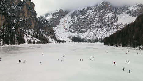 turistas caminando en el lago congelado braies con montañas nevadas de dolomita en el fondo en trentino, italia