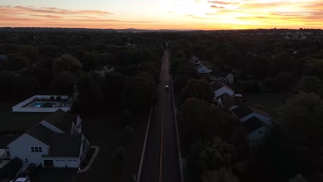 reverse aerial dolly backward shot of cars traveling on quiet road through neighborhood in america