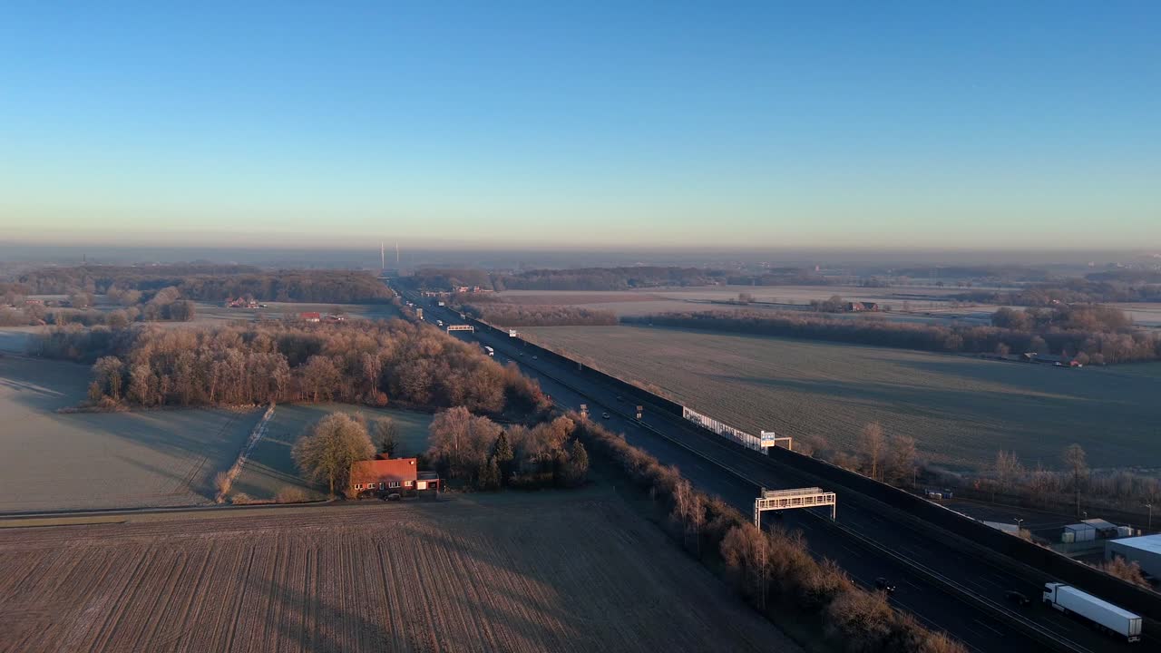 Traffic on german autobahn intersection during frosty winter day at sunrise time. Farm House and frozen fields at dawn. Aerial descend drone wide shot.