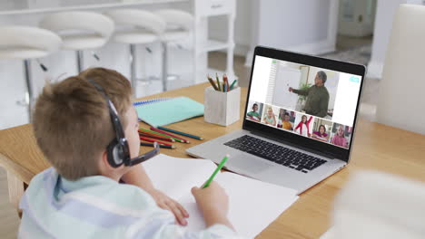 schoolboy using laptop for online lesson at home, with diverse teacher and class on screen