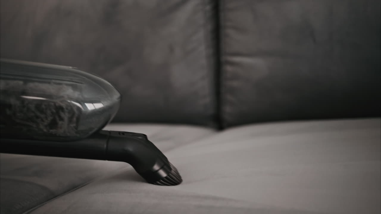 Close up of a small vacuum cleaning a grey couch