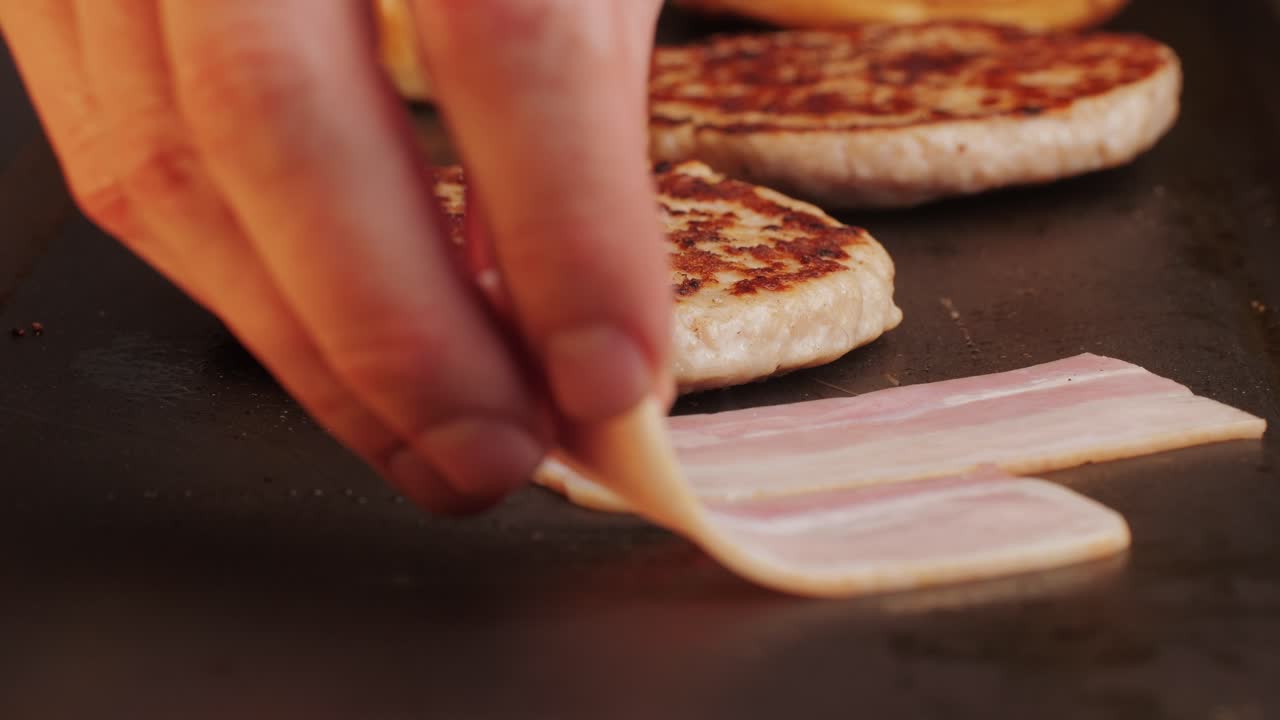 Cooking American fat smash burger and bacon slice on grill close-up. Chiken or fish cutlet smashing by burger press. The chef in kitchen of the restaurant making cutlets for burgers - smash burger beefsteak. Fast and street food concept. High quality 4k footage