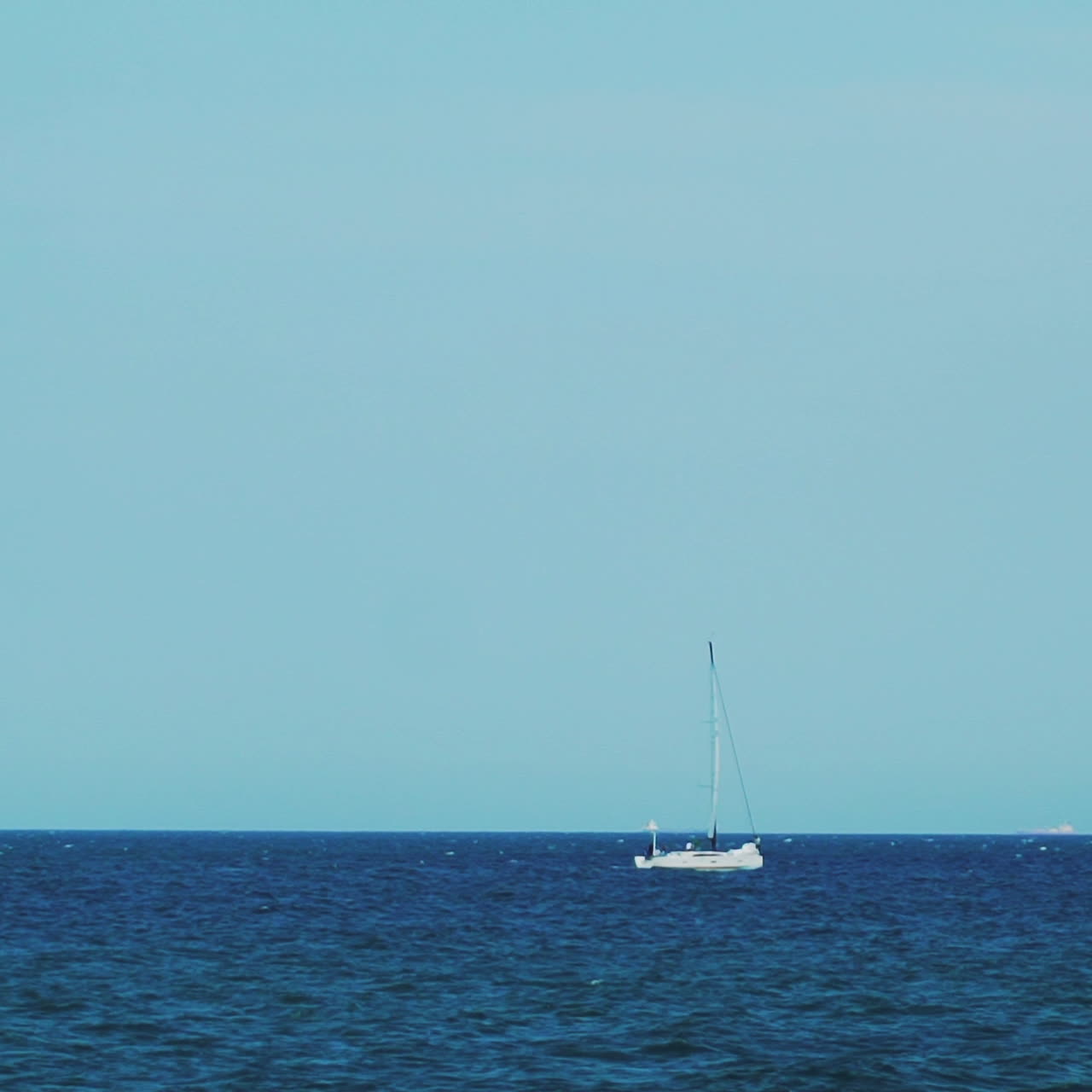 The yacht is under sail floats in the sea. On the horizon are seen cargo ships