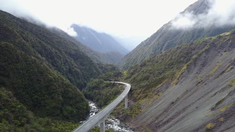 aerial-tracking-shot-of-a-road-with-Green-forest-and-Rocky-mountains