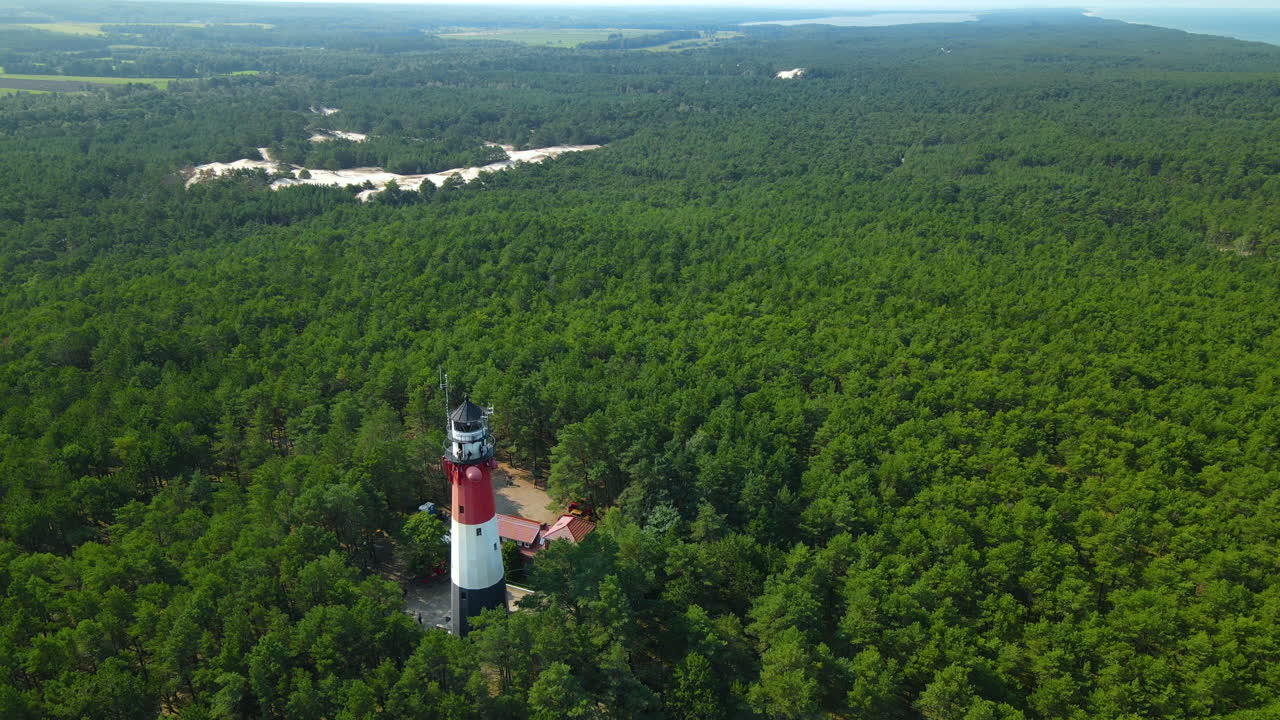 드론은 스틸로 등대와 그 주변의 푸른 숲에서 천천히 빠져나옵니다 - 발트해의 폴란드 해안에 있는 오세트닉에 위치한 등대, 사시노 마을 근처