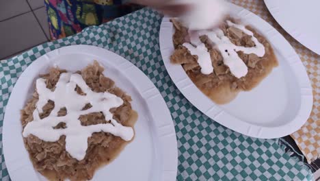 Pouring-sour-cream-and-cheese-on-green-chilaquiles