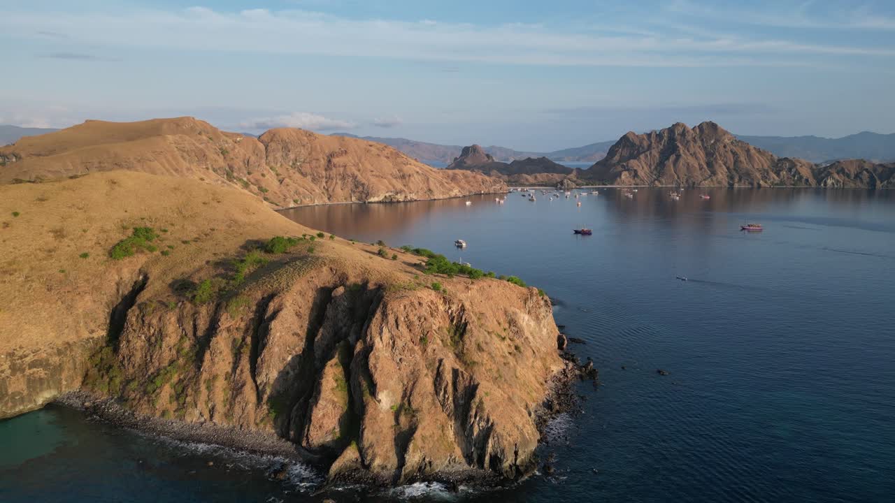 드론이 상승하고 앞으로 이동하여 많은 배가 정박한 보호된 만을 드러니다.