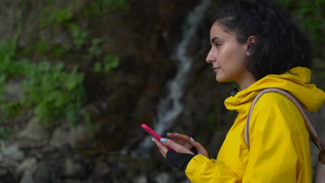 woman using phone near a waterfall in nature