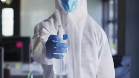 trabajador de la salud con ropa de protección y máscara facial rociando desinfectante en una oficina moderna