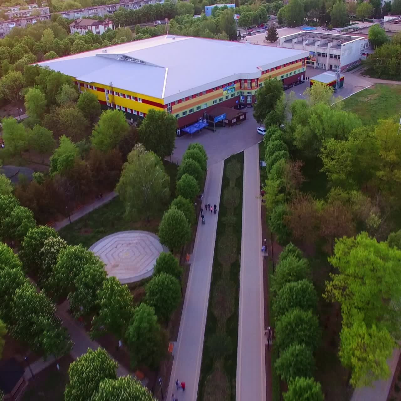 Green town park zone with artificial pond. Walking roads leading to the big shopping mall. Aerial view