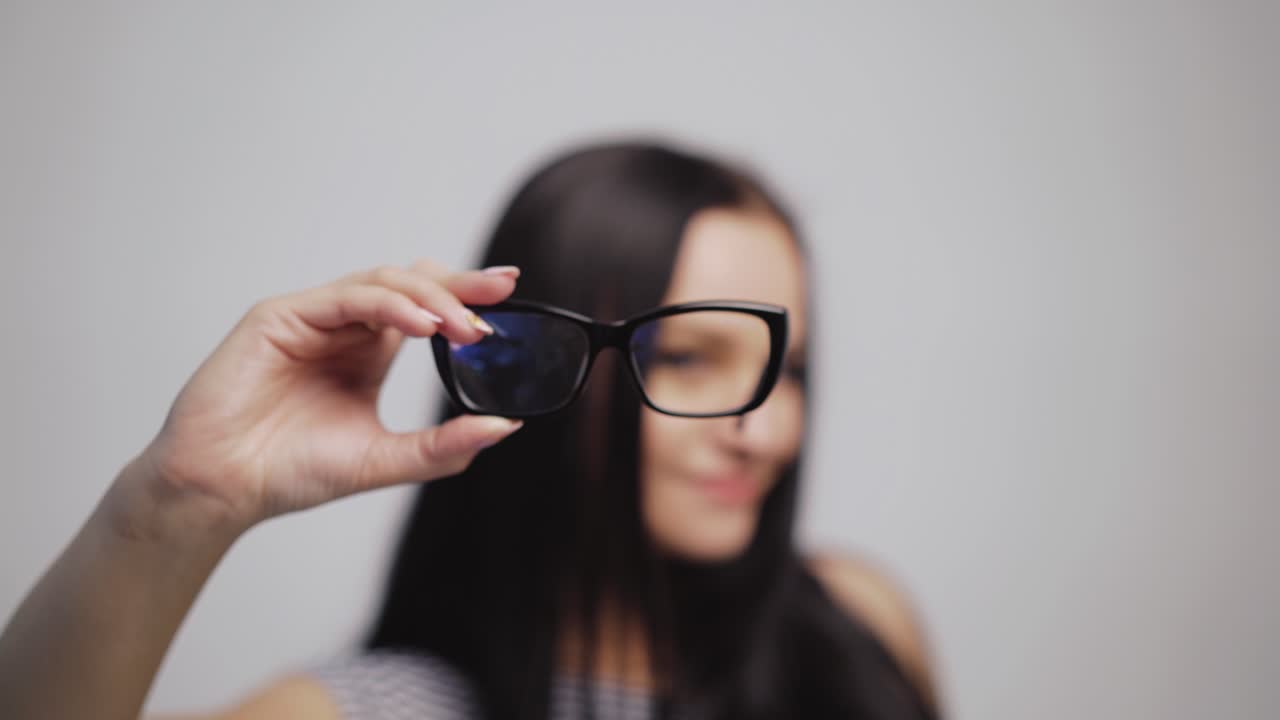 Pretty woman shows from left to right stylish eyeglasses and puts them on with blur background. Fashionable glasses in the hand of dark-haired female. Close-up