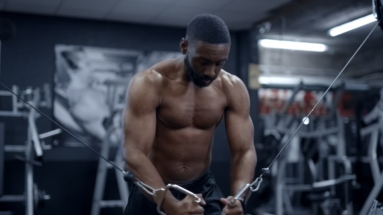 An african american man performs cable chest flys shirtless