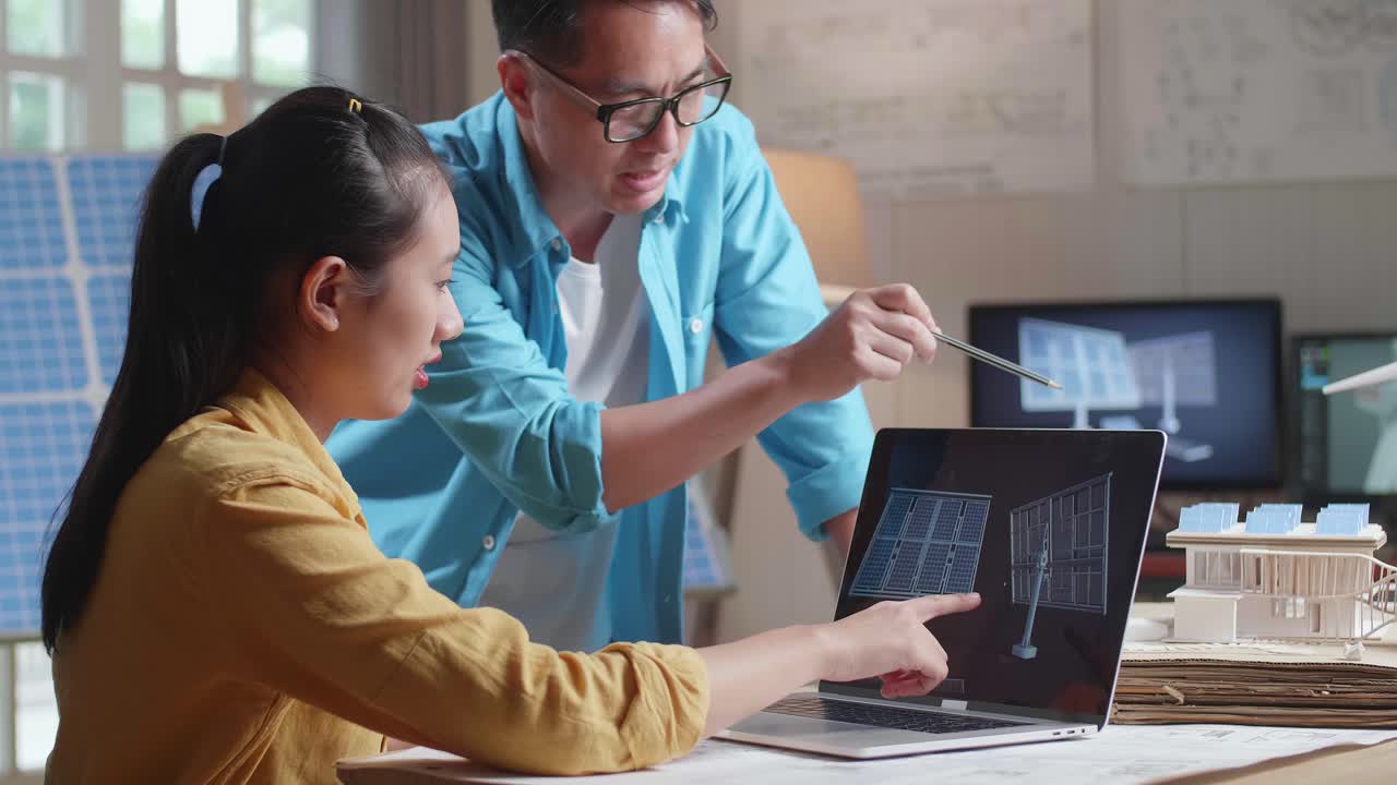 un hombre y una mujer asiáticos discuten sobre la célula solar en una computadora portátil junto al modelo de una pequeña casa con panel solar y turbina eólica