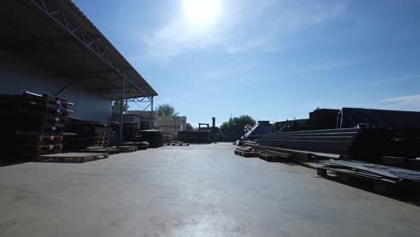 open air warehouse with euro pallets, packed material, metal corners and beams. camera movement from the factory through the gate to the street