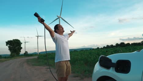 progressive man with his ev car and wind turbine as concept of renewable energy.